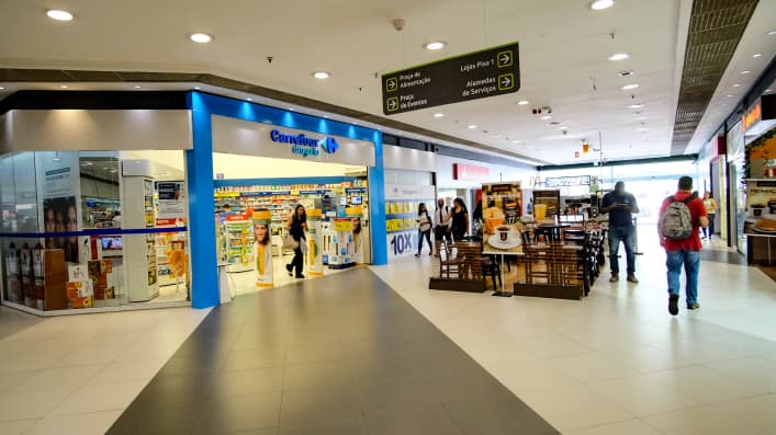Imagem de um corredor de shopping, apresentando a entrada das lojas Carrefour em cor azul